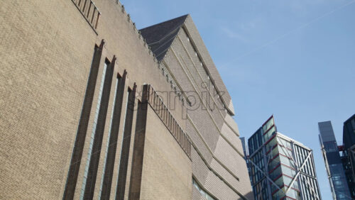 Low-angle view of Tate Modern’s distinct brick design alongside sleek modern buildings in London’s South Bank area, London, England - Starpik Stock