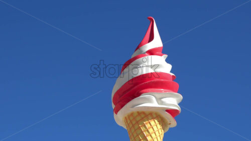 Low angle view of a large decorative red-and-white swirl ice cream cone sign against a clear blue - Starpik Stock