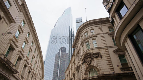 Low angle view of modern and classic buildings on a city street lined with trees and shops in London, England - Starpik Stock