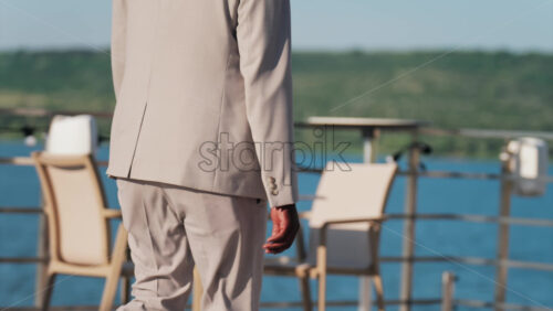 Man in beige suit walking on a scenic terrace with a view of a calm body of water - Starpik Stock