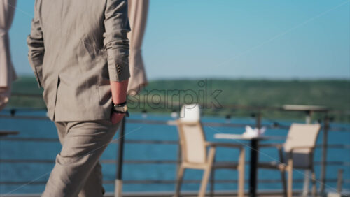 Man in beige suit walking past patio umbrellas on sunny terrace - Starpik Stock