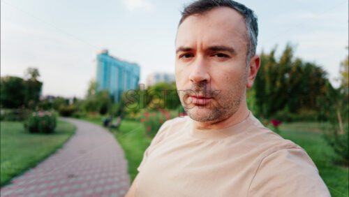 Man standing in a green city park, gesturing and speaking directly to the camera - Starpik Stock