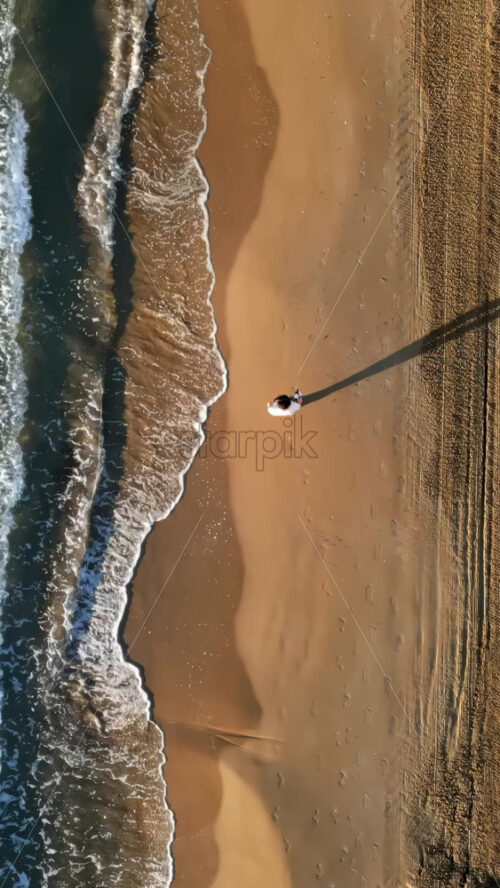 Man walking on the beach with waves hitting the shore in Alicante, Spain. Vertical - Starpik Stock