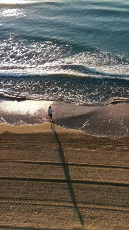 Man walking on the beach with waves hitting the shore in Alicante, Spain. Vertical - Starpik Stock