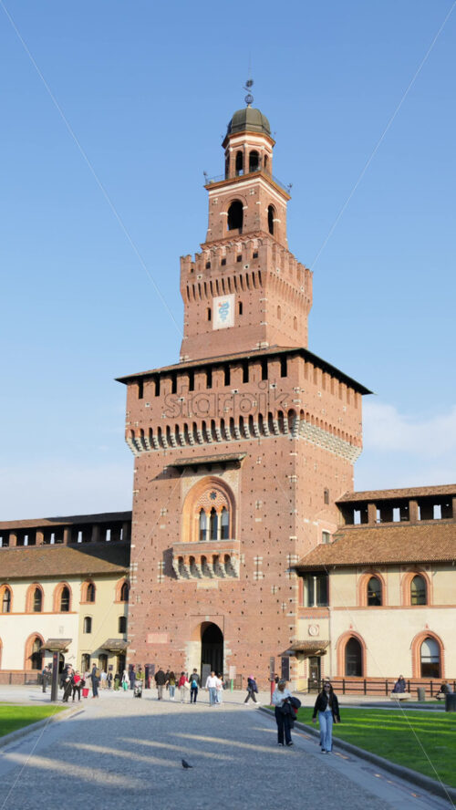 Milan, Italy – March 20, 2025: People walking at the Sforzesco Castle, near the Filarete Tower in daylight. Vertical - Starpik Stock