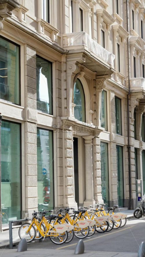 Milan, Italy – March 20, 2025: People walking by yellow, parked bicycles on the street - Starpik Stock