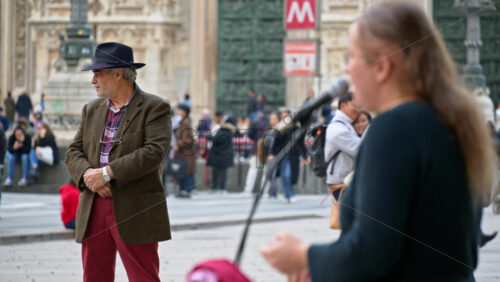 Milan, Italy – March 22, 2025: Man listening to a woman singing in the Duomo Square in daylight - Starpik Stock