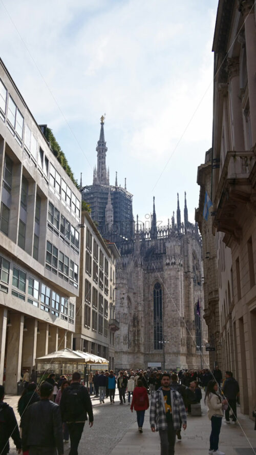 Milan, Italy – March 22, 2025: Side view of the Duomo with people walking through the square in daylight. Vertical - Starpik Stock