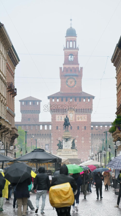 Milan, Italy – March 22, 2025: View of people walking by the Filarete Tower on a rainy day. Vertical - Starpik Stock