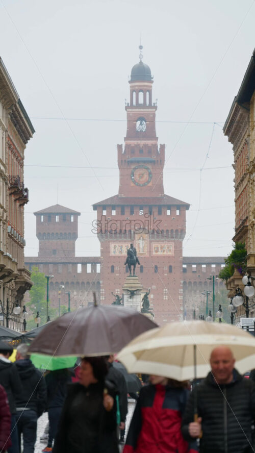 Milan, Italy – March 22, 2025: View of people walking by the Filarete Tower on a rainy day. Vertical - Starpik Stock