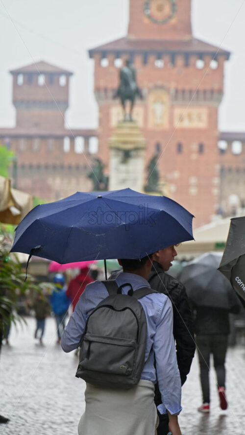 Milan, Italy – March 22, 2025: View of people walking by the Filarete Tower on a rainy day. Vertical - Starpik Stock