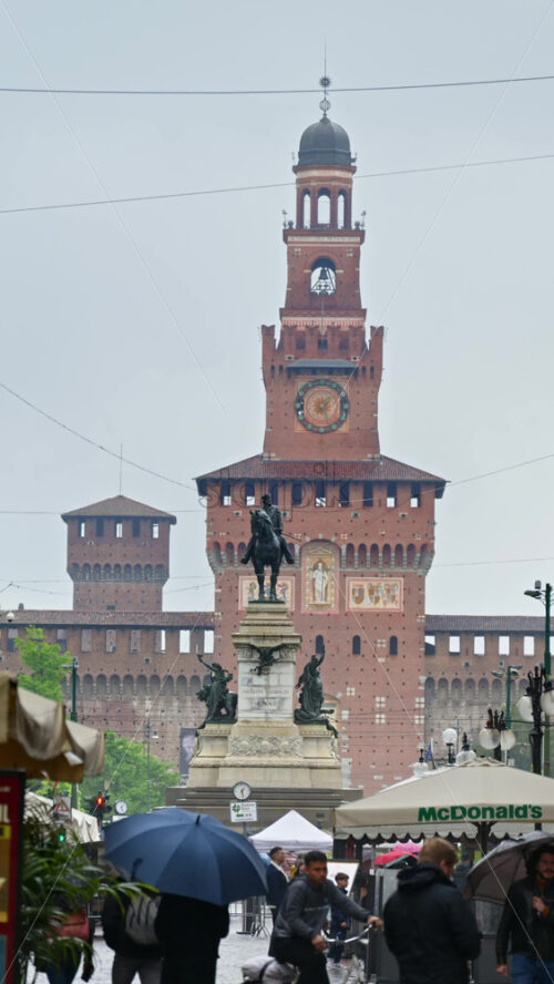 Milan, Italy – March 22, 2025: View of people walking by the Filarete Tower on a rainy day. Vertical - Starpik Stock