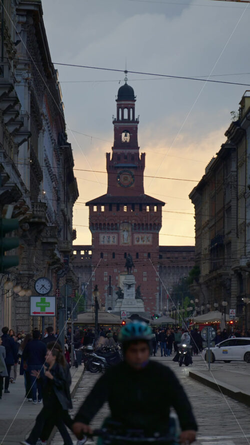 Milan, Italy – March 22, 2025: View of the Filarete Tower between buildings with people walking in the evening. Vertical - Starpik Stock