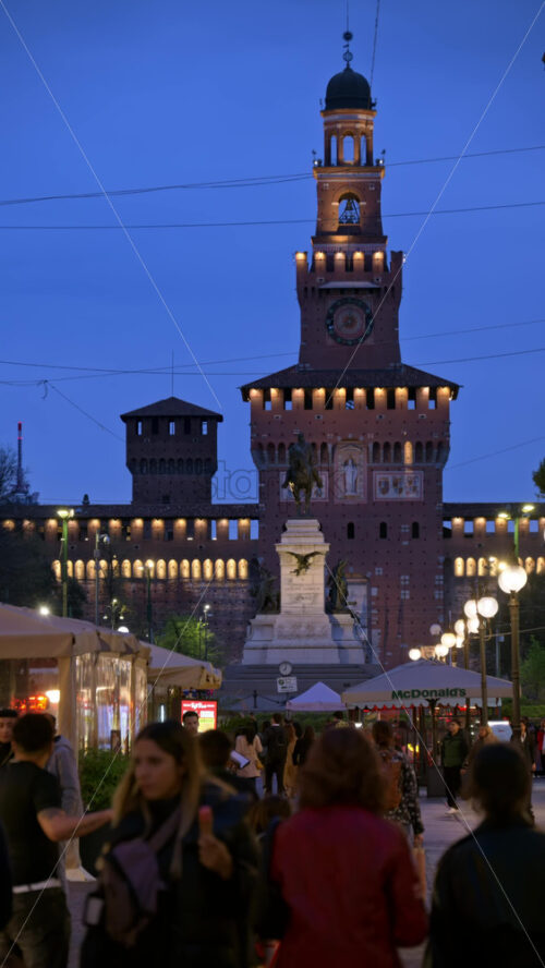 Milan, Italy – March 22, 2025: View of the Filarete Tower between buildings with people walking in the evening. Vertical - Starpik Stock