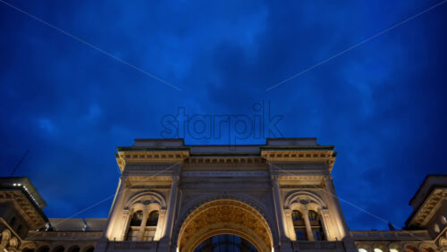 Milan, Italy – March 22, 2025: View of the Vittorio Emanuele II Gallery entrance from the Duomo square in the evening with blue hour sky - Starpik Stock