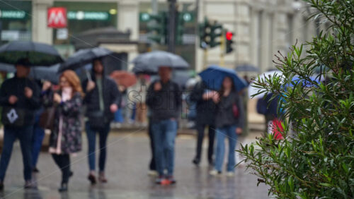 Milan, Italy – March 23, 2025: Blurred view of people holding umbrellas walking in the rain on thee street in Milan, Italy - Starpik Stock
