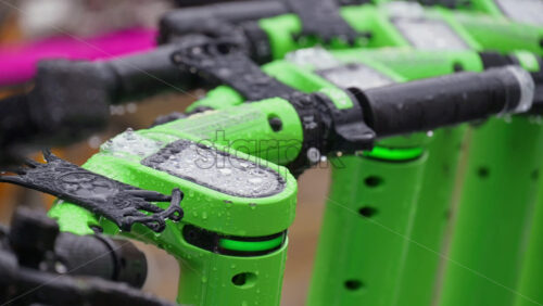 Milan, Italy – March 23, 2025: Close up of green electric scooters parked on the street in the rain in daylight - Starpik Stock