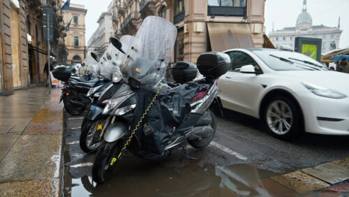 Milan, Italy – March 23, 2025: People and cars moving on the street near parked motorcycles in the rain - Starpik Stock