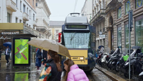 Milan, Italy – March 23, 2025: People getting on a yellow tram on a rainy day - Starpik Stock