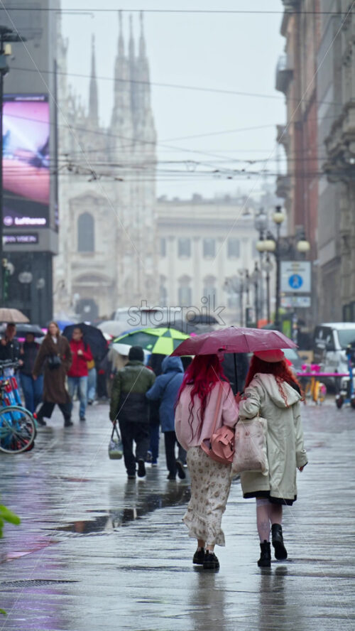 Milan, Italy – March 23, 2025: People holding umbrellas walking in the rain on thee street in Milan, Italy. Vertical - Starpik Stock