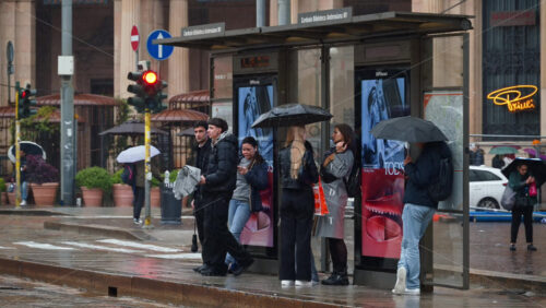 Milan, Italy – March 23, 2025: People waiting at the station, golding umbrellas in the rain - Starpik Stock