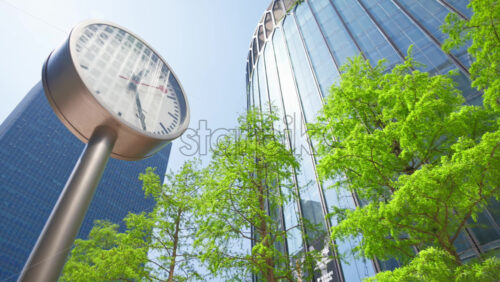 Modern clock on a pole with a building and trees on the background in Canary Wharf - Starpik Stock