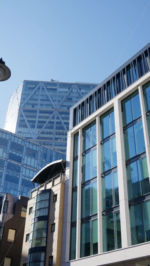Modern glass skyscrapers of London’s financial district reflecting the blue sky next to historic architecture. Vertical - Starpik Stock