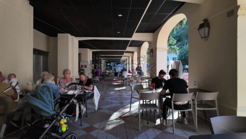 Monaco City, Monaco – July 18, 2025: People sitting at tables under a covered colonnade with arches in daylight - Starpik Stock