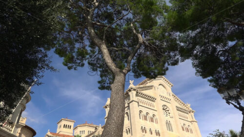 Monaco City, Monaco – July 4, 2025: Low angle view of the facade of the Cathedral of Our Lady Immaculate framed by green trees - Starpik Stock