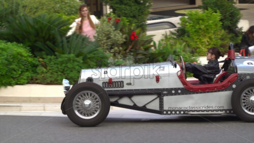 Monte Carlo, Monaco – July 4, 2025: Side view of a woman driving a retro-style silver sports car from Monaco Classic Rides through the courtyard of the Monte Carlo Casino - Starpik Stock