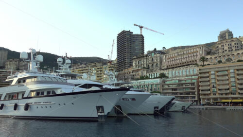 Monte Carlo, Monaco – July 4, 2025: Yachts and launches tied up near the modern tiered Yacht Club building, with luxury residences along the quay - Starpik Stock