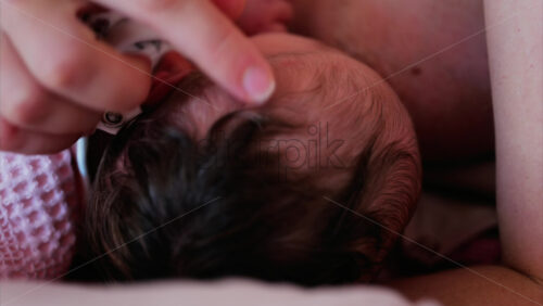 Mother gently cradling newborn’s head while breastfeeding in a quiet, intimate moment - Starpik Stock