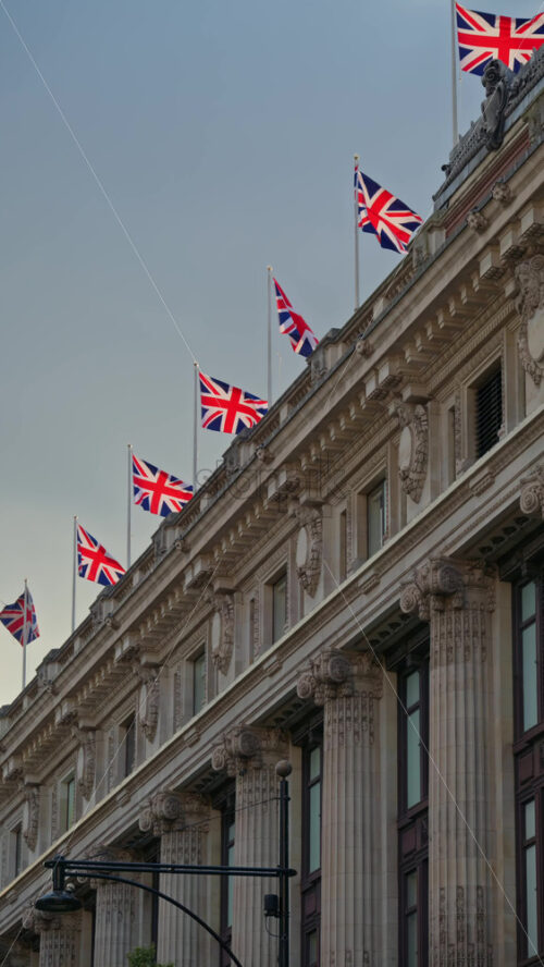 Multiple Union Jack flags waving atop a classic London building under a cloudy sky in London, England. Vertical - Starpik Stock