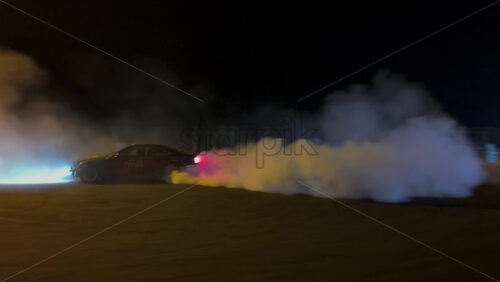 Mures, Romania – July 19, 2025: A fast sports car performing a drift in an open lot illuminated by bright streetlights on a rainy night at the RoDrift competition - Starpik Stock