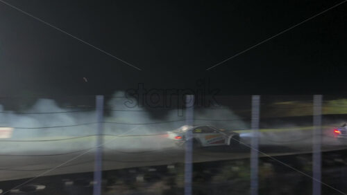 Mures, Romania – July 19, 2025: Two cars drifting at high speed on the Transilvania Motor Ring, race track at night, with headlights and tire smoke at the RoDrift competition - Starpik Stock