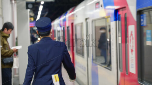 Nara, Japan – April 10, 2025: A uniformed train conductor walking along the platform next to a moving train with people waiting at the station - Starpik Stock