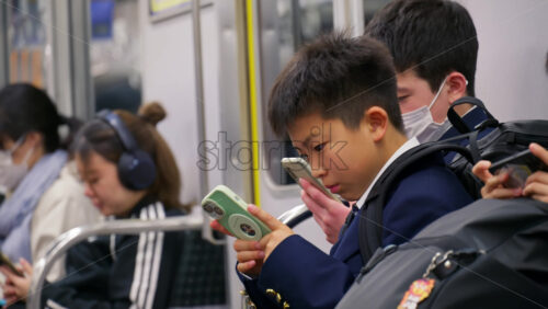 Nara, Japan – April 10, 2025: Japanese children looking at their phones while sitting on the train - Starpik Stock