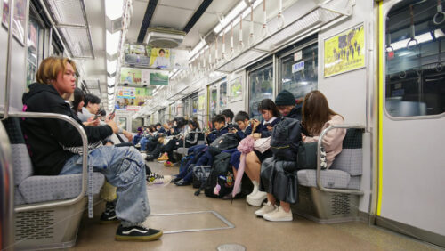 Nara, Japan – April 10, 2025: Japanese people sleeping and looking at their phones while sitting on the train. Translation: “Looking for bus drivers” - Starpik Stock