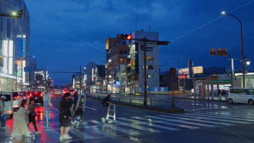 Nara, Japan – April 10, 2025: People crossing the street and cars moving through the city on a rainy evening. Translation: “Coin parking, Bus stop to Nara and Yamatoji” - Starpik Stock