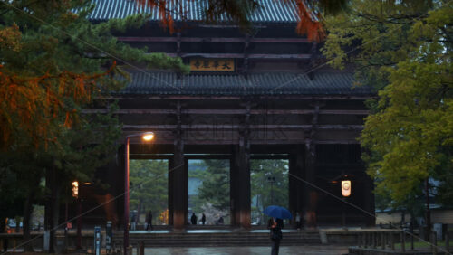 Nara, Japan – April 10, 2025: Tourist walking in the rain at the Todai-ji Namdaimon, Grand South Gate, the main gate of the Todai-ji Temple. Translation: “Great Kegon Temple” - Starpik Stock