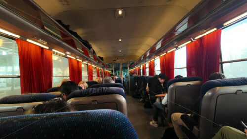 Nice, France – August 15 2025: View inside a train carriage with passengers seated, orange curtains, and luggage stored above - Starpik Stock