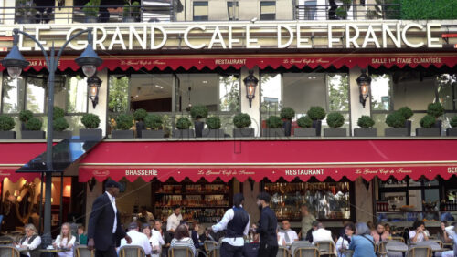 Nice, France – July 3, 2025: Busy outdoor seating at Le Grand Cafe de France with patrons dining under red awnings and pedestrians walking by on a sunny day - Starpik Stock