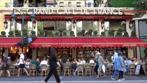 Nice, France – July 3, 2025: Busy outdoor seating at Le Grand Cafe de France with patrons dining under red awnings and pedestrians walking by on a sunny day - Starpik Stock