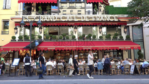 Nice, France – July 3, 2025: Busy outdoor seating at Le Grand Cafe de France with patrons dining under red awnings and pedestrians walking by on a sunny day - Starpik Stock