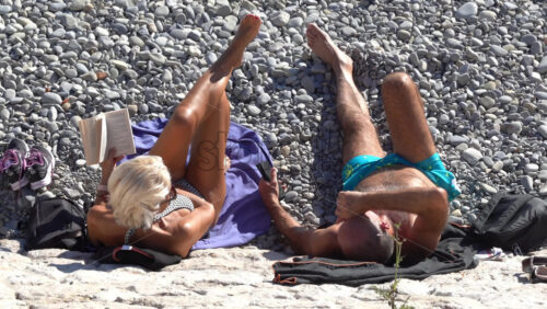 Nice, France – July 3, 2025: Overhead view of a couple lounging on a pebble beach, the woman reading a book while the man scrolls on his phone - Starpik Stock