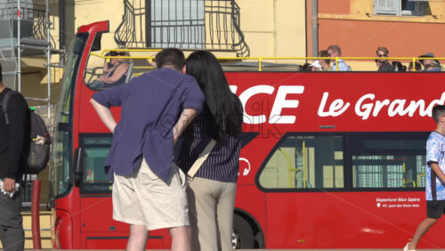 Nice, France – July 3, 2025: Tourists walking past a bright red sightseeing bus with Nice Le Grand Tour written on it - Starpik Stock