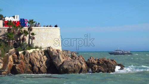 Nice, France – July 3, 2025: View of the I Love Nice sign on the Promenade des Anglais, with tourists enjoying the lookout and a passenger boat cruising across the Mediterranean Sea - Starpik Stock