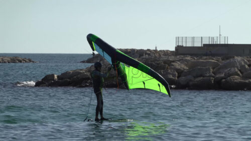 Nice, France – July 5, 2025: A windsurfer gliding across the deep blue Mediterranean sea using a vibrant green and blue sail - Starpik Stock