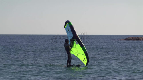 Nice, France – July 5, 2025: A windsurfer gliding across the deep blue Mediterranean sea using a vibrant green and blue sail - Starpik Stock