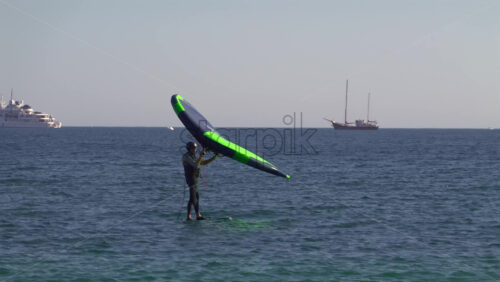 Nice, France – July 5, 2025: A windsurfer gliding across the deep blue Mediterranean sea using a vibrant green and blue sail - Starpik Stock